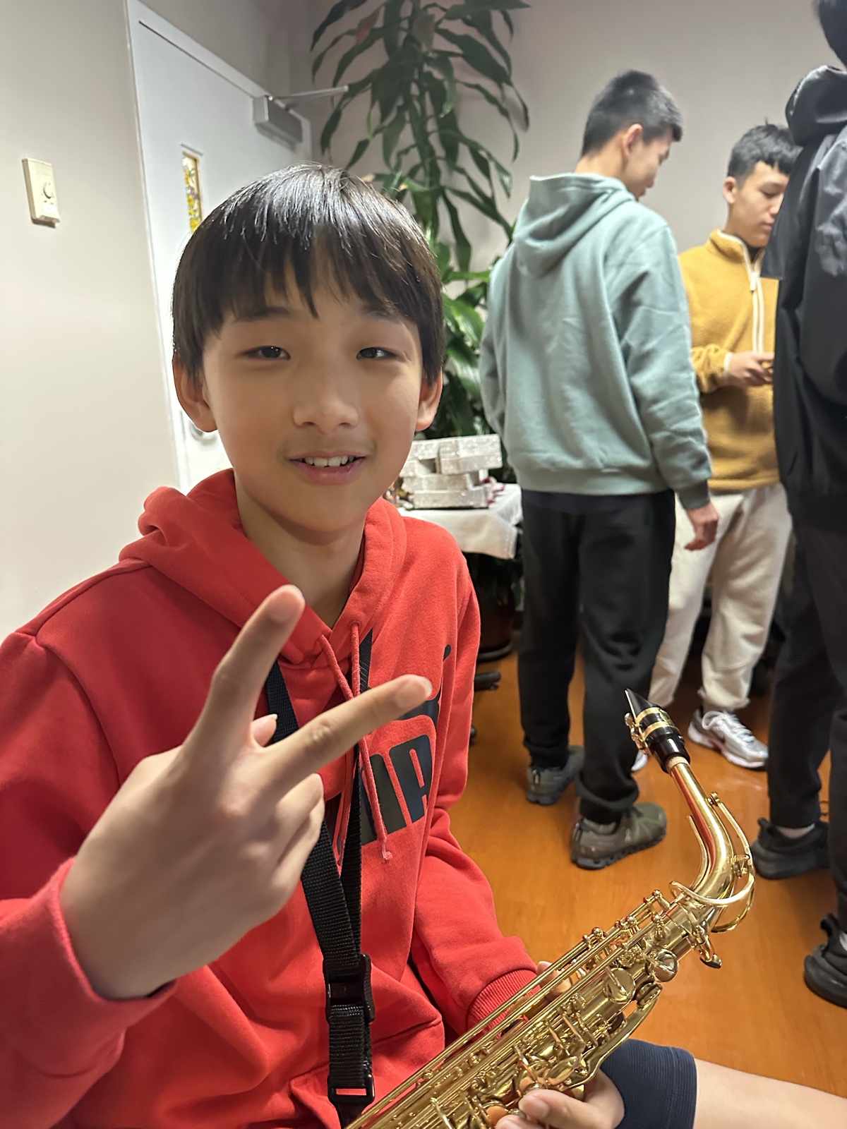 A student in a red hoodie smiling and holding a saxophone before going on stage