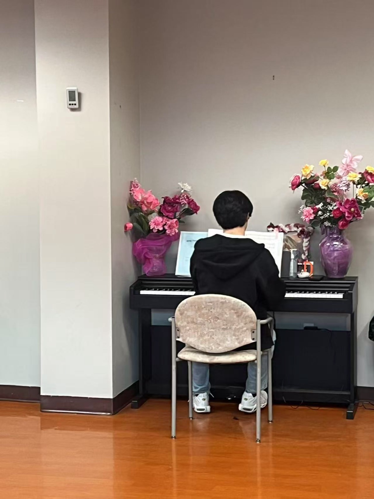 A student playing the piano at the senior center, framed by two bouquets of flowers