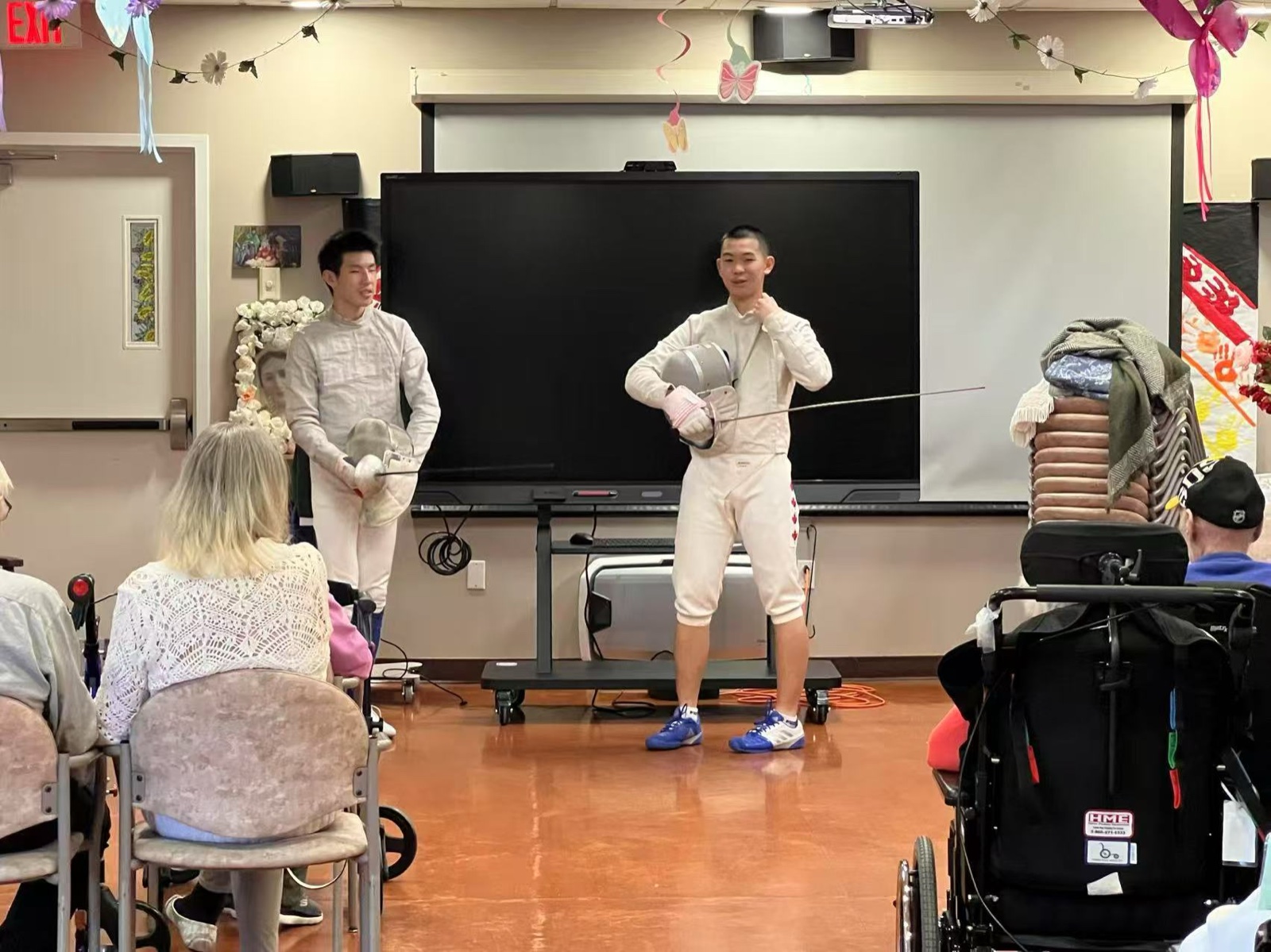 Two student volunteers in fencing whites holding masks, ready to demonstrate for residents
